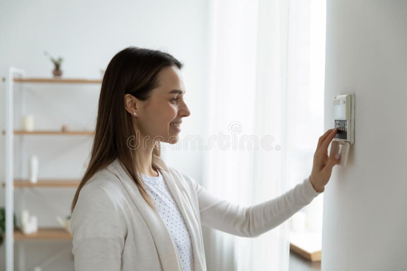 Uśmiechnięta kobieta regulująca stopnie ustawia temperaturę komfortową za pomocą termostatu