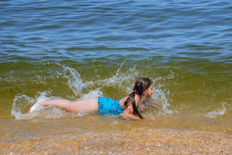 Uśmiechnięta mała dziewczynka kłaść w wodzie na plażowym wybrzeżu mnie ocean fotografia stock Uśmiechnięta mała dziewczynka kłaść w wodzie na plażowym wybrzeżu mnie ocean fotografia stock