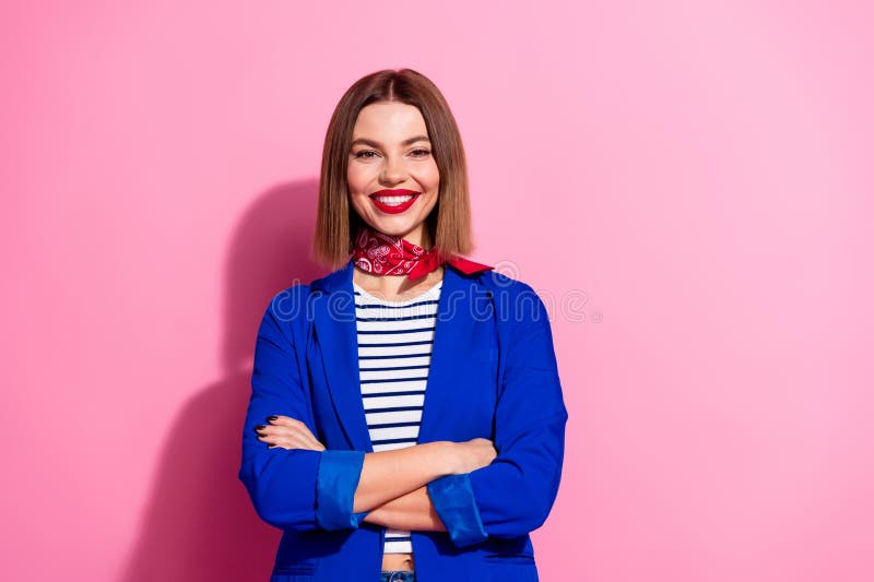 Uśmiechnięta młoda kobieta w stylowej niebieskiej kurtce z paskowym górnym i czerwonym szalikiem pozornym na różowym tle zdjęcia royalty free