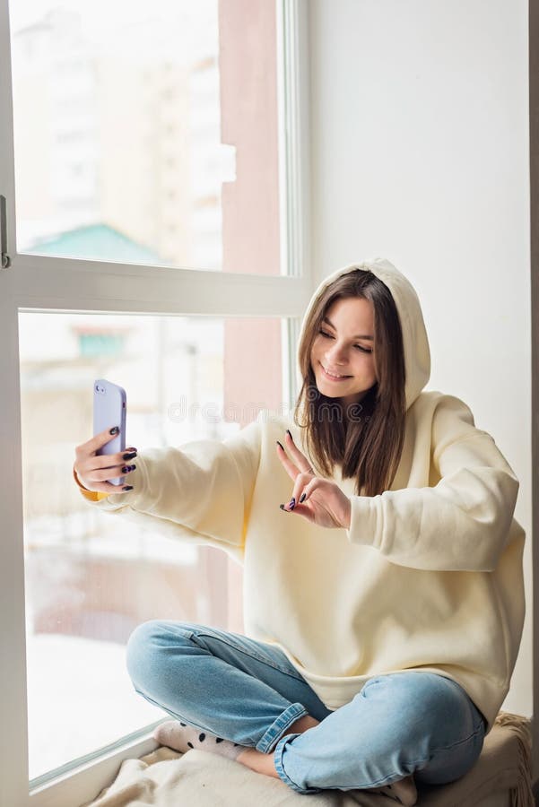 Uśmiechnięta młoda nastolatka telewizja z telefonem komórkowym, rozmawiająca z rodziną przyjaciół, zabierająca selfie dla mediów s fotografia royalty free