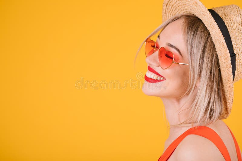 Uśmiechnięta piękna blondynki kobieta w starw kapeluszu na rozochoconym żółtym tle Serce kształtujący różowi okulary przeciwsłone fotografia royalty free Uśmiechnięta piękna blondynki kobieta w starw kapeluszu na rozochoconym żółtym tle Serce kształtujący różowi okulary przeciwsłone fotografia royalty free