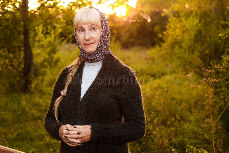 Uśmiechnięta pięćdziesięcioletnia kobieta patrzeje kamerę w lecie przy zmierzchem w szaliku na jej kardiganie i głowie zdjęcie royalty free Uśmiechnięta pięćdziesięcioletnia kobieta patrzeje kamerę w lecie przy zmierzchem w szaliku na jej kardiganie i głowie zdjęcie royalty free