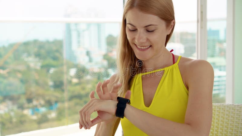 Uśmiechnięta szczęśliwa kobieta w kolor żółty sukni obsiadaniu na balkonie Używać jej smartwatch, przesyłanie wiadomości z przyja