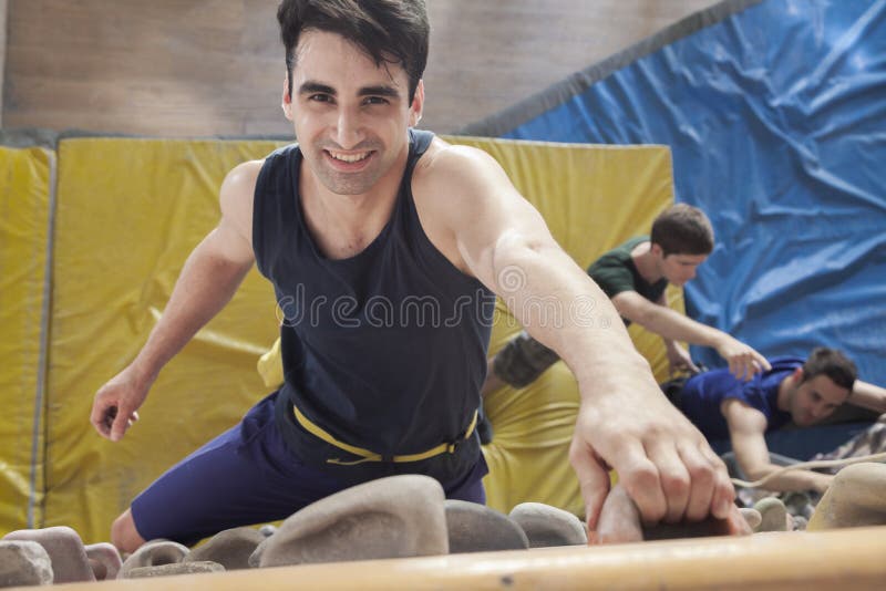 Uśmiechniętego młodego człowieka wspinaczkowy up wspinaczkowa ściana w salowym wspinaczkowym gym, bezpośrednio above zdjęcia stock Uśmiechniętego młodego człowieka wspinaczkowy up wspinaczkowa ściana w salowym wspinaczkowym gym, bezpośrednio above zdjęcia stock