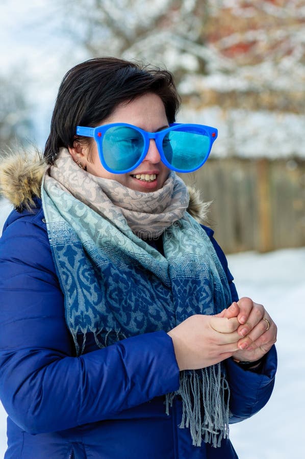 Uśmiechniętej brunetki dorosła dziewczyna stoi z kolei trzy czwarte w dużej błazen niebieskiej marynarce z szalikiem i szkłach zdjęcie stock Uśmiechniętej brunetki dorosła dziewczyna stoi z kolei trzy czwarte w dużej błazen niebieskiej marynarce z szalikiem i szkłach zdjęcie stock