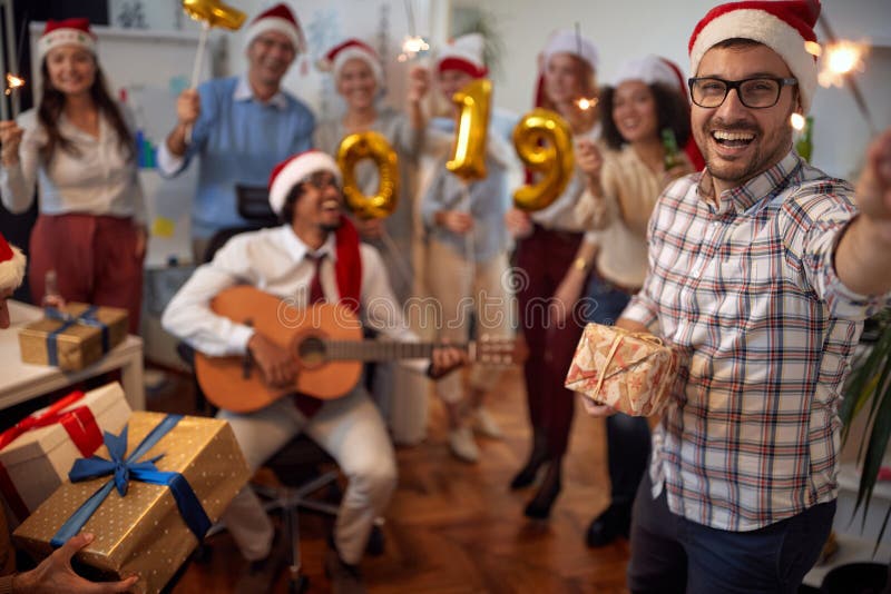Uśmiechnięty biznesowy mężczyzna zabawę w Santa kapeluszu przy Xmas przyjęciem z jego kolegami fotografia stock Uśmiechnięty biznesowy mężczyzna zabawę w Santa kapeluszu przy Xmas przyjęciem z jego kolegami fotografia stock