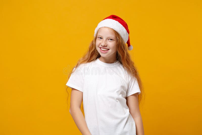 Uśmiechnięty mały imbir dzieciak santa dziewczyna 1213 lat w białej koszuli świątecznej kapelusz odizolowany na żółtym tle