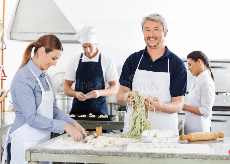 Uśmiechnięty Męski szef kuchni Z kolegami Przygotowywa makaron zdjęcia stock Uśmiechnięty Męski szef kuchni Z kolegami Przygotowywa makaron zdjęcia stock