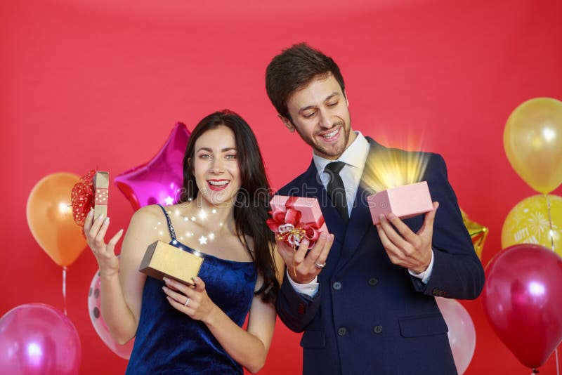 Uśmiechnięty mężczyzna i piękna kobieta otwierający pudełko z magicznym światłem na czerwonym tle w święta i wesołego Nowego Roku zdjęcie stock Uśmiechnięty mężczyzna i piękna kobieta otwierający pudełko z magicznym światłem na czerwonym tle w święta i wesołego Nowego Roku zdjęcie stock