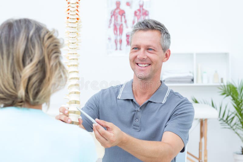 Uśmiechnięty physiotherapist pokazuje kręgosłupa modela jego pacjent obrazy stock Uśmiechnięty physiotherapist pokazuje kręgosłupa modela jego pacjent obrazy stock