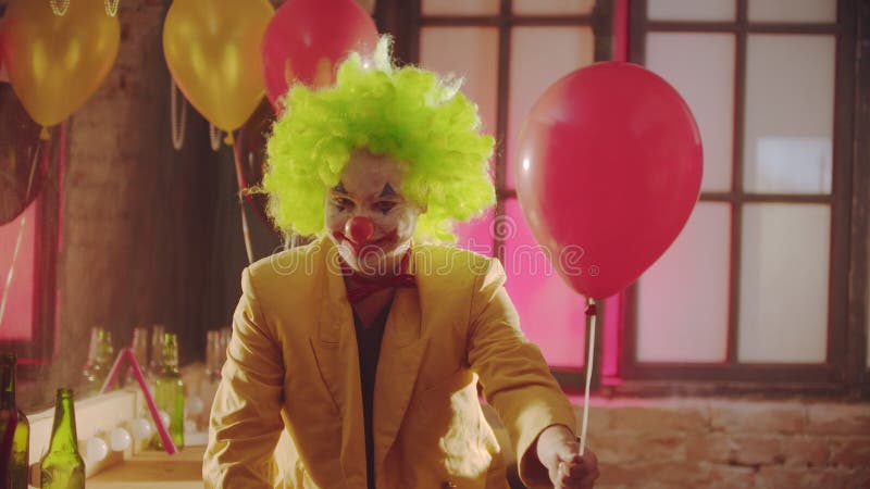 Uśmiechnięty, przerażający klaun w kolorowym kostiumie wręcza piłkę widzom i uśmiecha się