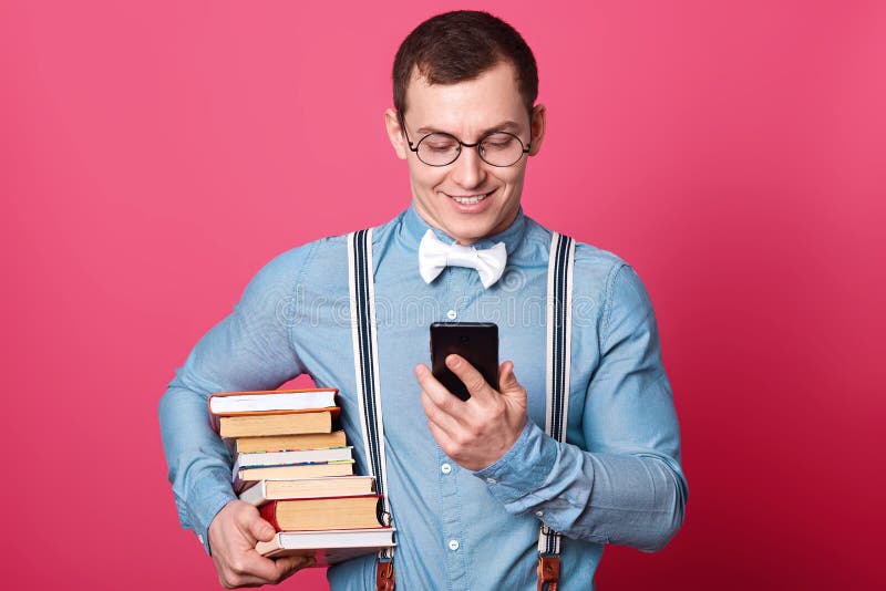 Uśmiechnięty uczeń z stertą książki, ubierająca koszula w jeden brzmieniu, suspenders i łęku krawat, recives wiadomość z dobre wi obraz stock Uśmiechnięty uczeń z stertą książki, ubierająca koszula w jeden brzmieniu, suspenders i łęku krawat, recives wiadomość z dobre wi obraz stock
