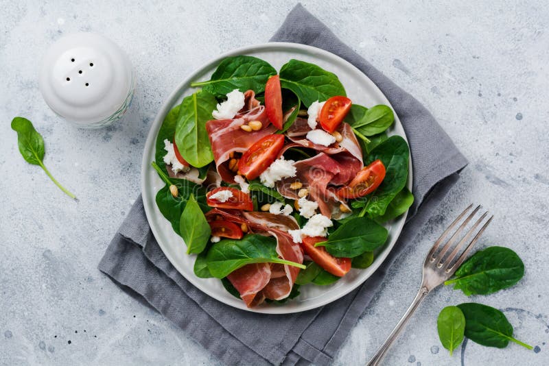 V?rsallad med spenat, den k?rsb?rsr?da tomaten, mozzarella, s?rjer muttrar och skinka med olivolja i en enkel keramisk platta royaltyfri fotografi V?rsallad med spenat, den k?rsb?rsr?da tomaten, mozzarella, s?rjer muttrar och skinka med olivolja i en enkel keramisk platta royaltyfri fotografi