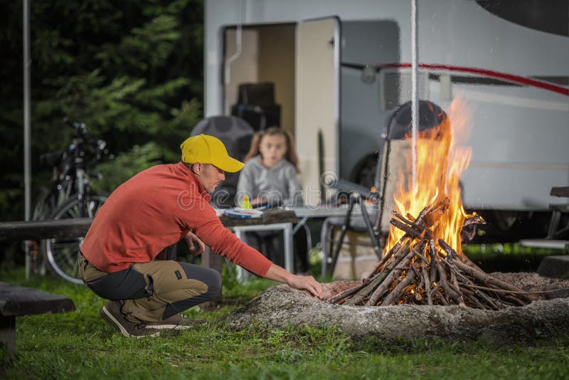 RV Camping Campfire in Front of Motorhome Pitch. Summer Vacation with Motorhome. Caucasian Family. RV Camping Campfire in Front of Motorhome Pitch. Summer Vacation with Motorhome. Caucasian Family