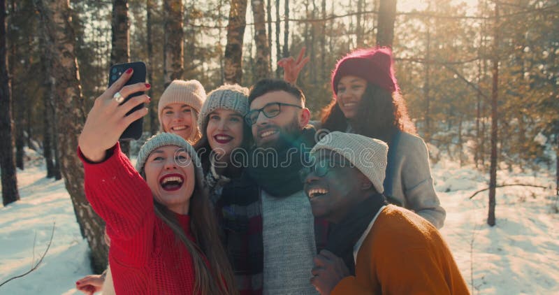 Vacaciones de invierno. alegres y felices amigos multiétnicos toman foto selfie juntos en soleada y nevada cámara lenta de los bos almacen de metraje de vídeo