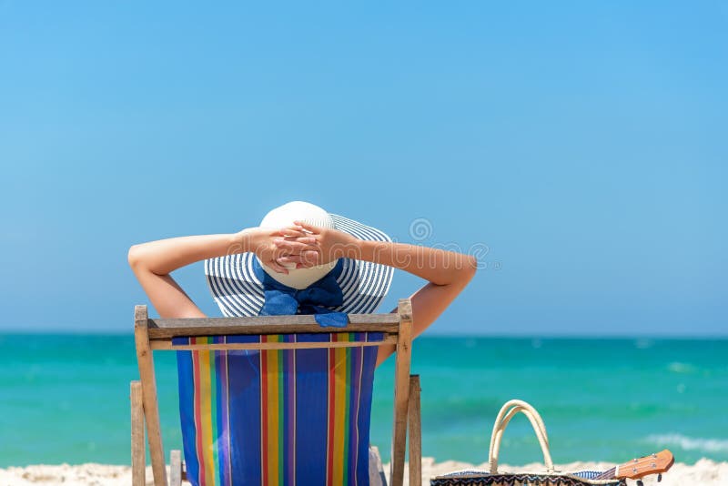 Vacanza di estate Bella giovane donna asiatica che si rilassa e felice sulla sedia di spiaggia con il succo della noce di cocco d