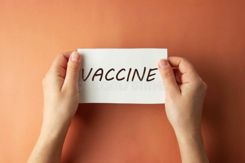 VACCINATION inscription. Woman holding paper with Vaccine lettering in hands isolated brown background. Top view stock photo VACCINATION inscription. Woman holding paper with Vaccine lettering in hands isolated brown background. Top view stock photo