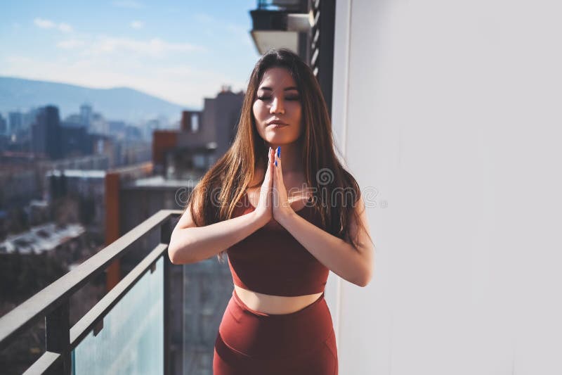 Vacker assisk leende, lämplig kvinna som gör yoga på solig balkong i idrottsdräkt. Ung lycklig dam på terace på sommaren arkivfoto