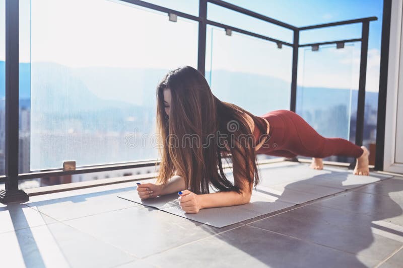 Vacker assisk leende, lämplig kvinna som gör yoga på solig balkong i idrottsdräkt. Ung lycklig dam på terace på sommaren royaltyfri foto