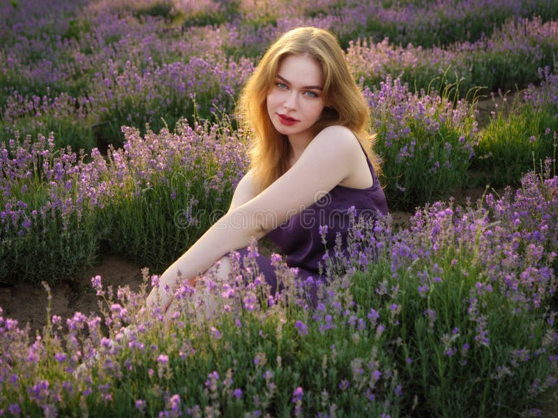 Vacker blond flicka med långt hår på ett lavenderfält på kvällen fotografering för bildbyråer