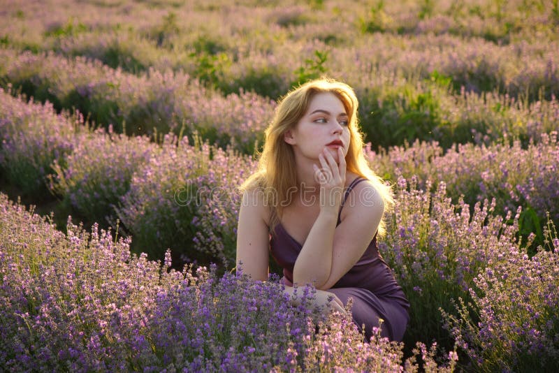 Vacker blond flicka med långt hår på ett lavenderfält på kvällen arkivfoto