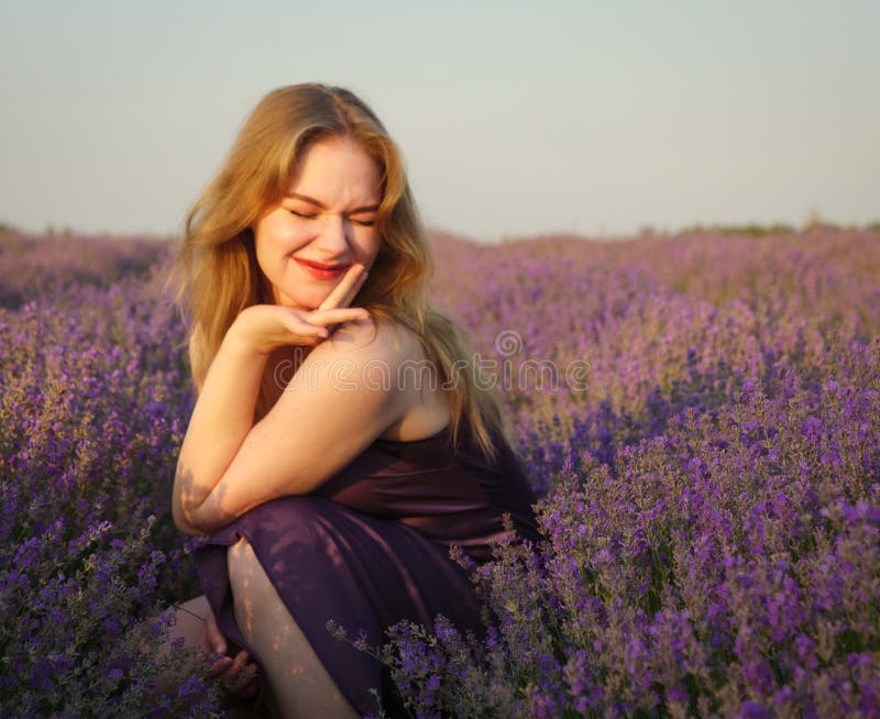 Vacker blond flicka med långt hår på ett lavenderfält på kvällen royaltyfri foto