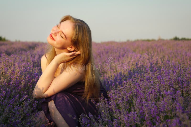 Vacker blond flicka med långt hår på ett lavenderfält på kvällen royaltyfri bild