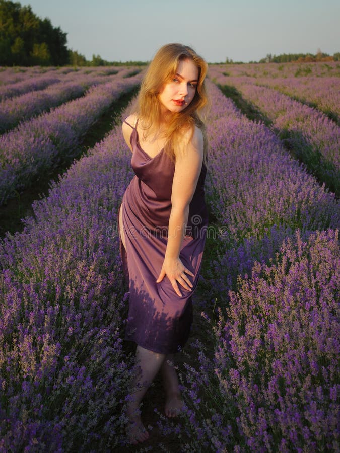 Vacker blond flicka med långt hår på ett lavenderfält på kvällen royaltyfri bild