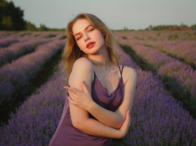 Vacker blond flicka med långt hår på ett lavenderfält på kvällen arkivbild