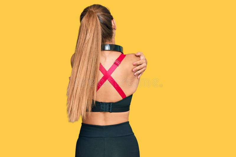 Vacker blond kvinna som bär gym kläder och som använder hörlurar som kramar sig själv glad och positiv bakifrån royaltyfri bild