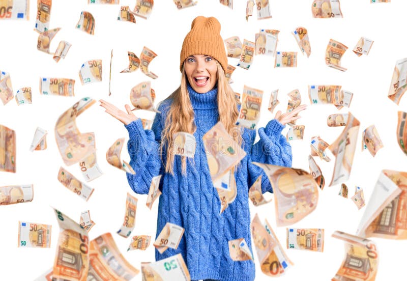 Beautiful caucasian woman with blonde hair wearing wool sweater and winter hat celebrating victory with happy smile and winner expression with raised hands. Beautiful caucasian woman with blonde hair wearing wool sweater and winter hat celebrating victory with happy smile and winner expression with raised hands