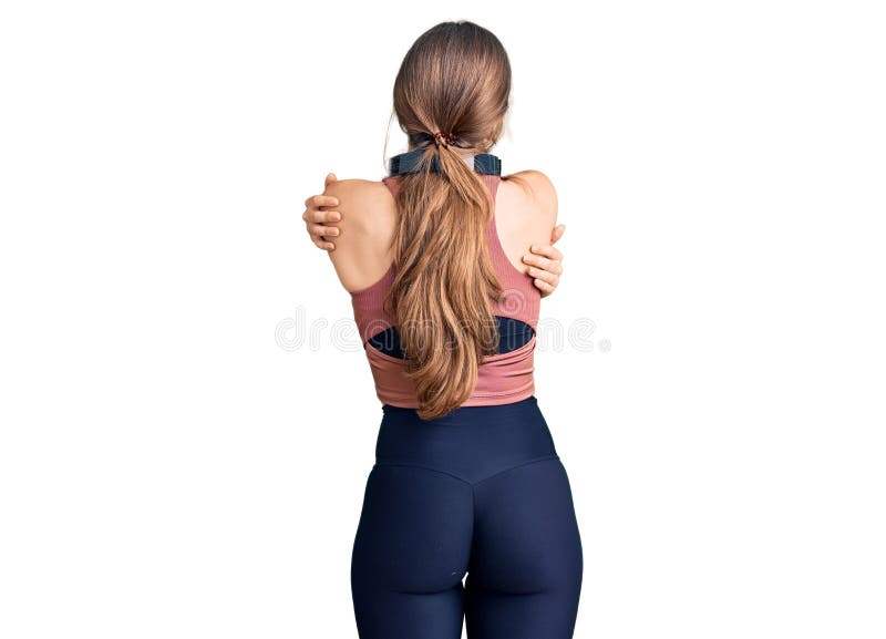 Vacker kaukasisk ung kvinna som bär gymnastikkläder och använder hörlurar som kramar sig själv lyckliga och positiva bakifrån arkivfoto