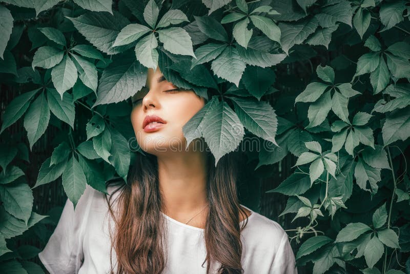 Vacker modemodellflicka som njuter av naturen och andas frisk luft i sommarträdgården över gröna blad bakgrund