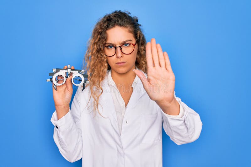 Vacker, okänd kvinna med blå ögon som håller optometriska glasögon över isolerad bakgrund med öppen hand och stoppskylt med öppen arkivfoto