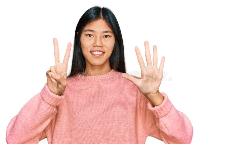 Vacker ung asiatisk kvinna som bär tillfällig vintertröja som visar och pekar upp med fingrar nummer sju medan hon ler royaltyfria foton