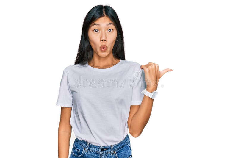 Vacker ung asiatisk kvinna som bär tillfällig vit t-skjorta förvånad över att med handfingret peka på sidan öppna munnen förbluffa fotografering för bildbyråer