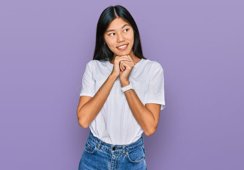 Vacker ung asiatisk kvinna som bär tillfällig vit t-skjorta och som skrattar nervöst och som är upphetsad med händer på huden och royaltyfri bild