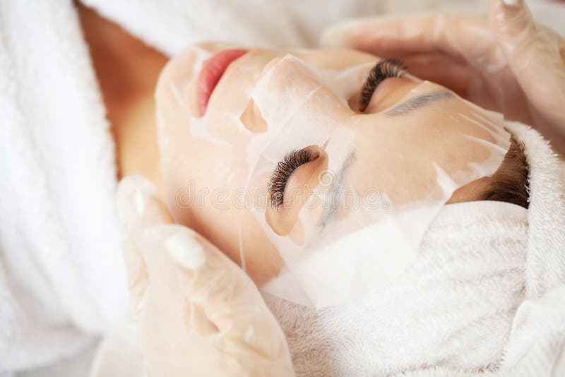 Vacker ung kvinna använder sig av ansiktsmask på ansiktet för skönhetspa.