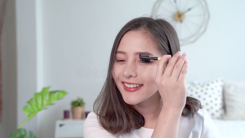 Vackra asiatiska kvinnor som bildar sig genom att använda en pensel för att applicera ögonbryn