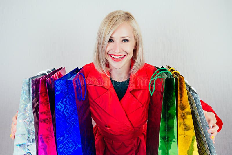 Vackra blonda kvinnliga shopahoar i en röd rock med shoppingväskor 'shopaholism och försäljning' fotografering för bildbyråer Vackra blonda kvinnliga shopahoar i en röd rock med shoppingväskor 'shopaholism och försäljning' fotografering för bildbyråer