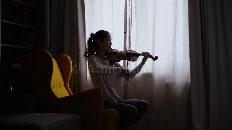 Vackra flickmusiker spelar i bakgrunden av ett fönster hemma