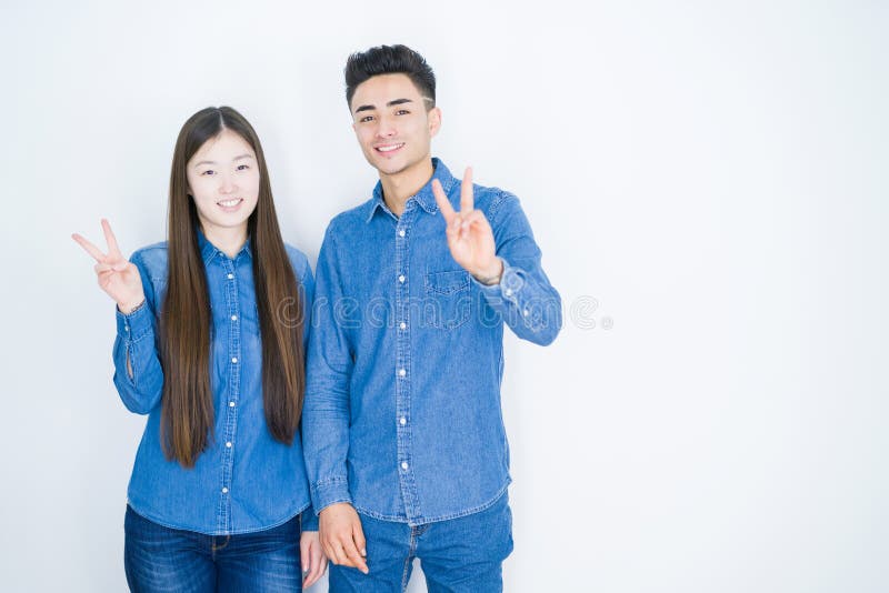 Vackra unga asiatiska par över vit, isolerad bakgrund leende med glad ansiktsvinkning vid kameran som gör segertecken royaltyfri fotografi
