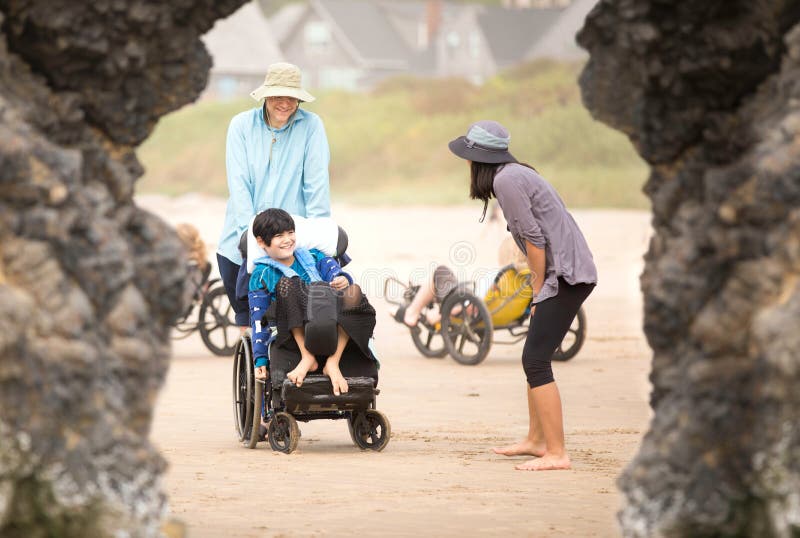 Caucasian Father with children on beach, talking. Young disabled son in wheelchair. Caucasian Father with children on beach, talking. Young disabled son in wheelchair