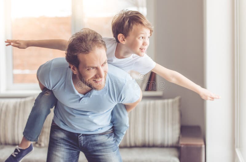 Father and son are smiling while spending time together. Little boy is sitting pickaback while imitating the flight. Father and son are smiling while spending time together. Little boy is sitting pickaback while imitating the flight