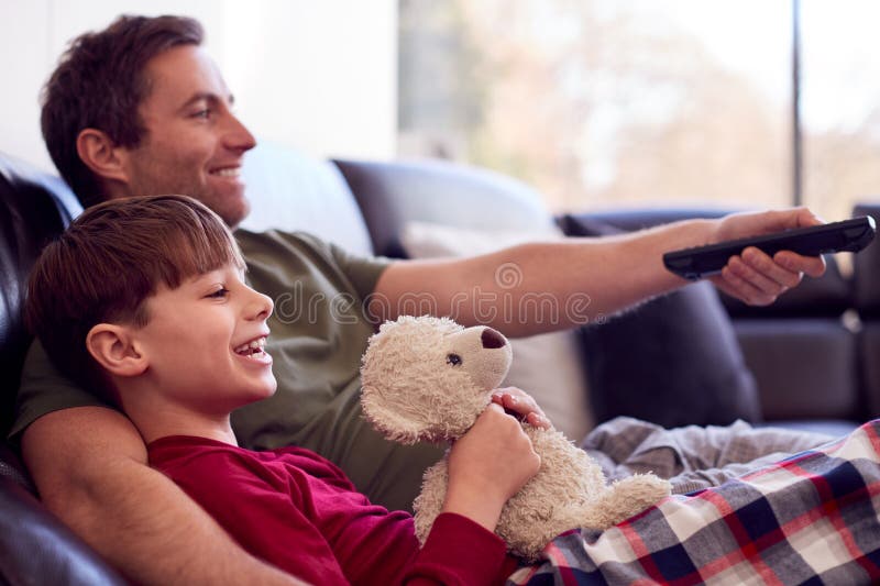 Father And Son With Toy Dog Sitting On Sofa In Pyjamas Together Watching TV. Father And Son With Toy Dog Sitting On Sofa In Pyjamas Together Watching TV