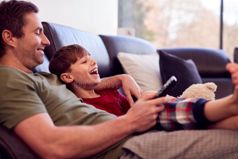 Father And Son With Toy Dog Sitting On Sofa In Pyjamas Together Watching TV. Father And Son With Toy Dog Sitting On Sofa In Pyjamas Together Watching TV