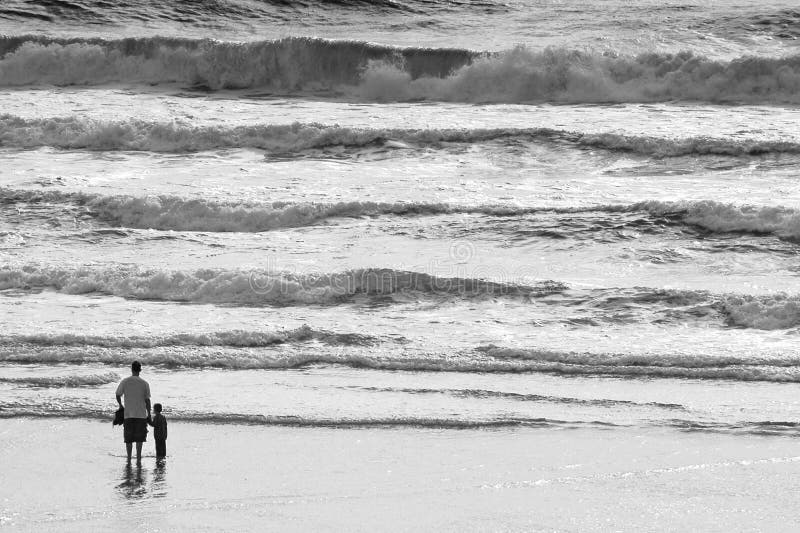 Vader en zoonsholdingshanden op het strand bij de vreedzame oceaan bij zonsondergang met golven stock foto Vader en zoonsholdingshanden op het strand bij de vreedzame oceaan bij zonsondergang met golven stock foto