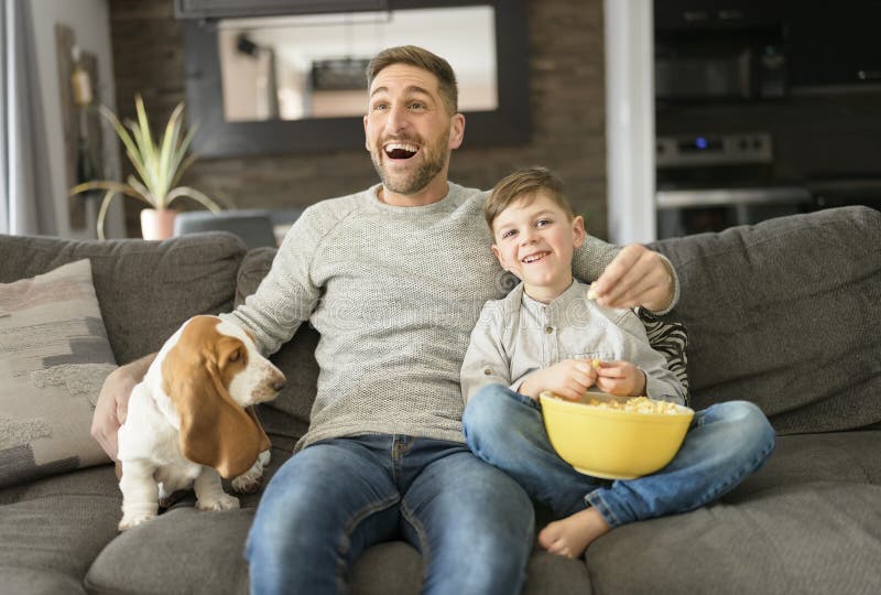 A Father or Godfather with Basset dog having fun on the living room At Home watching movie with popcorn. A Father or Godfather with Basset dog having fun on the living room At Home watching movie with popcorn