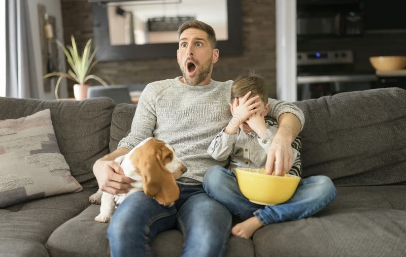 A Father or Godfather with Basset dog having fun on the living room At Home watching movie with popcorn look like afraid. A Father or Godfather with Basset dog having fun on the living room At Home watching movie with popcorn look like afraid