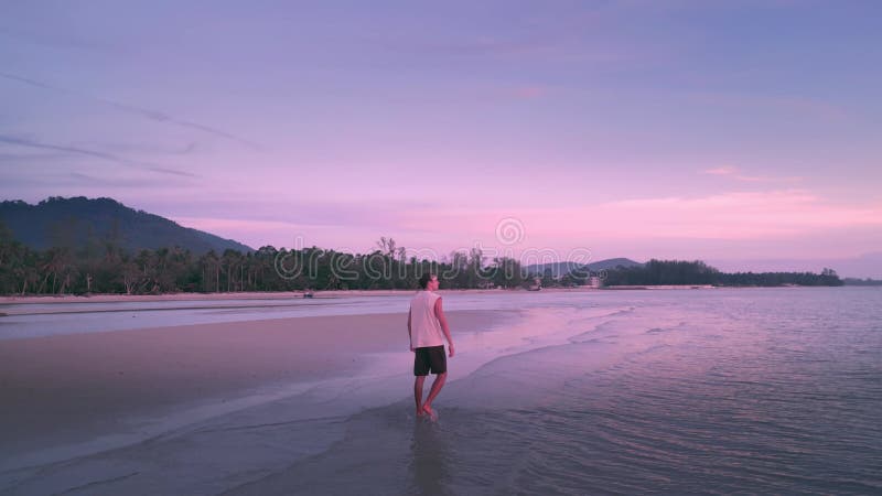 Vakantie mannelijke reiziger die op zeestrand loopt op een roze zonsondergang die vakantie ontspant zomer. kaukasus